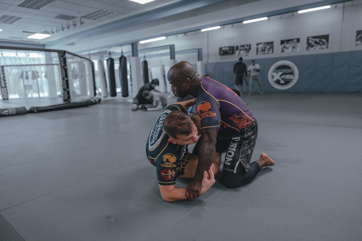 Two grapplers drilling guard retention movements on a gym mat