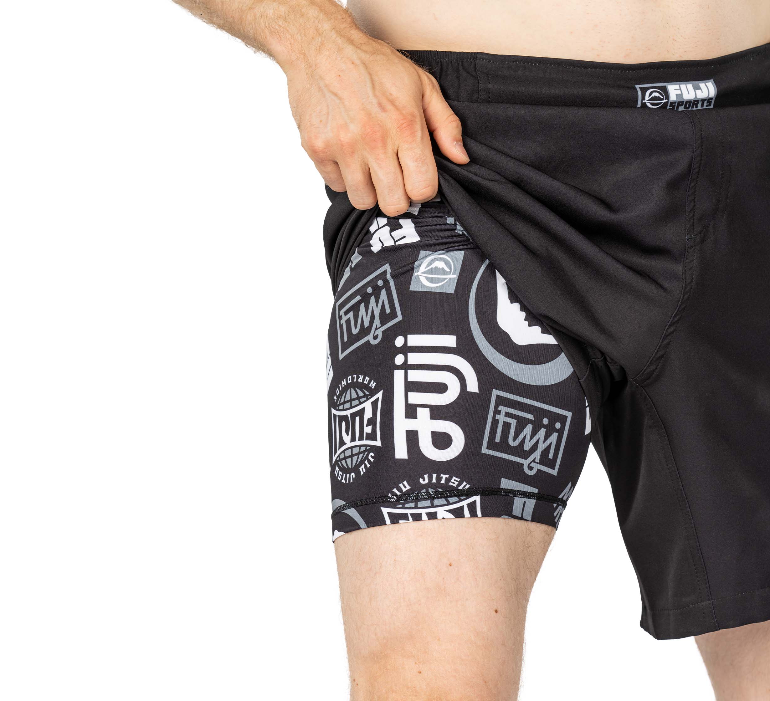 Someone lifts the outer layer of Ultimate Grappling Shorts Black to reveal matching black compression shorts underneath, both