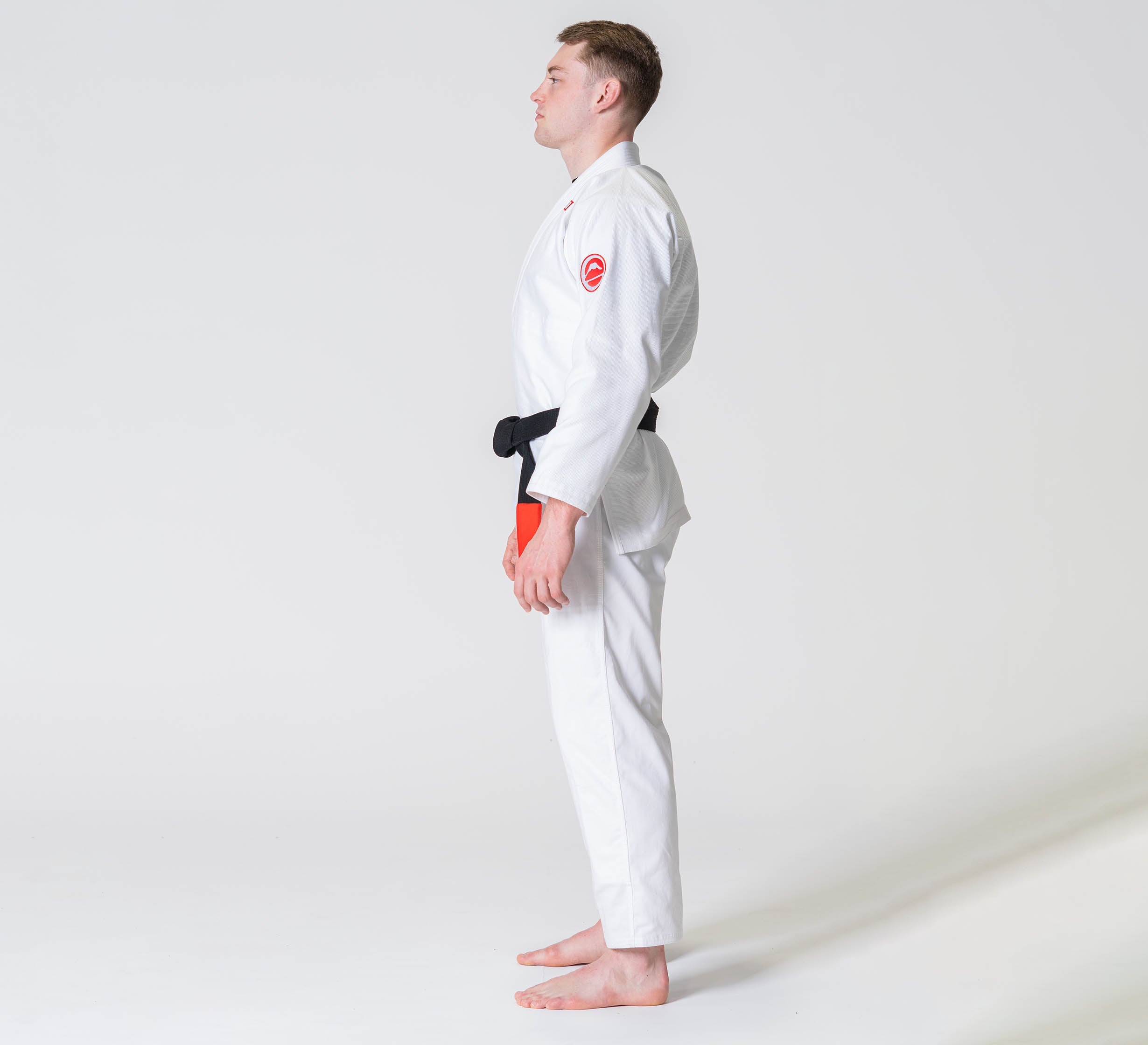 A person stands barefoot in a side profile pose wearing the Competition BJJ Gi White against a plain white background.