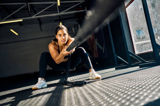 female athlete pulling a weighted sled in a gym. front view of a woman performing strength training exercise on a black gym f