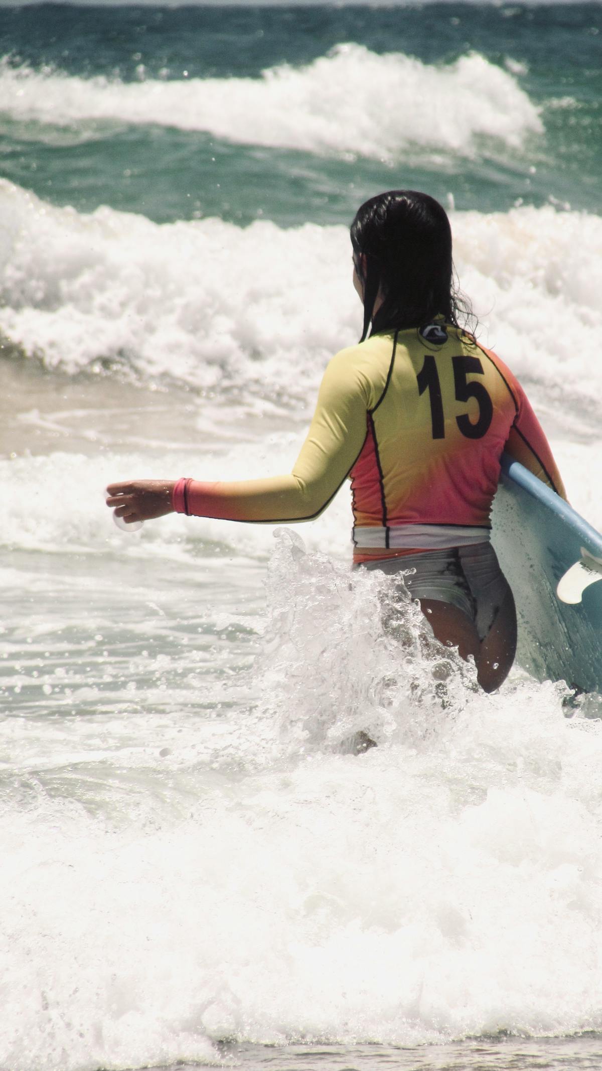 Female surfer in rashguard entering ocean waves