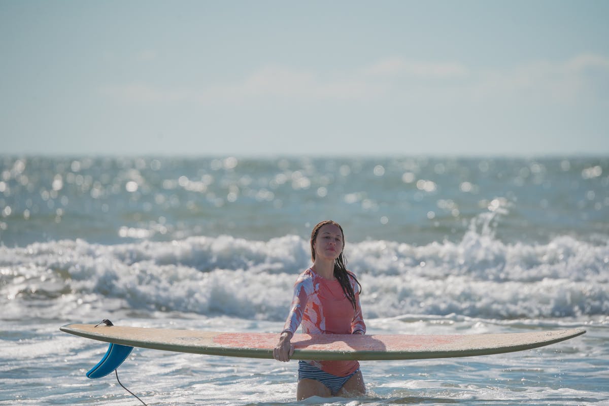 Woman in rashguard standing in ocean with surfboard