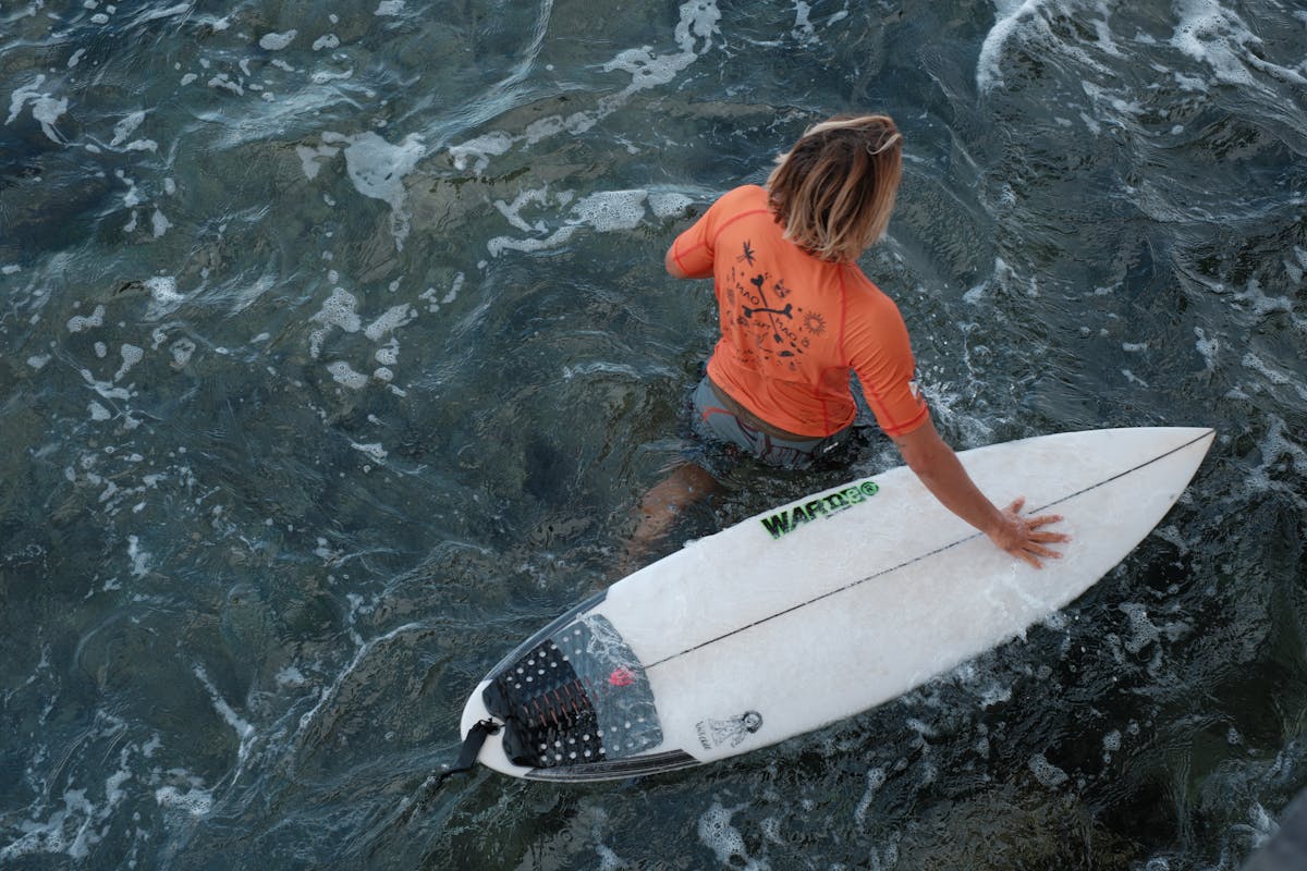 Surfer in orange rashguard preparing to ride waves
