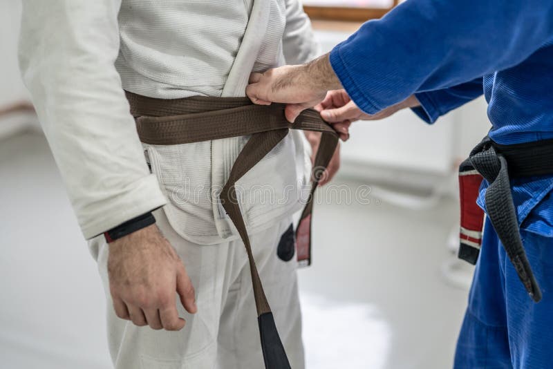 BJJ brazilian jui jutsu belt promotion close up on hands of unknown instructor black belt professor tie up brown belt on wais