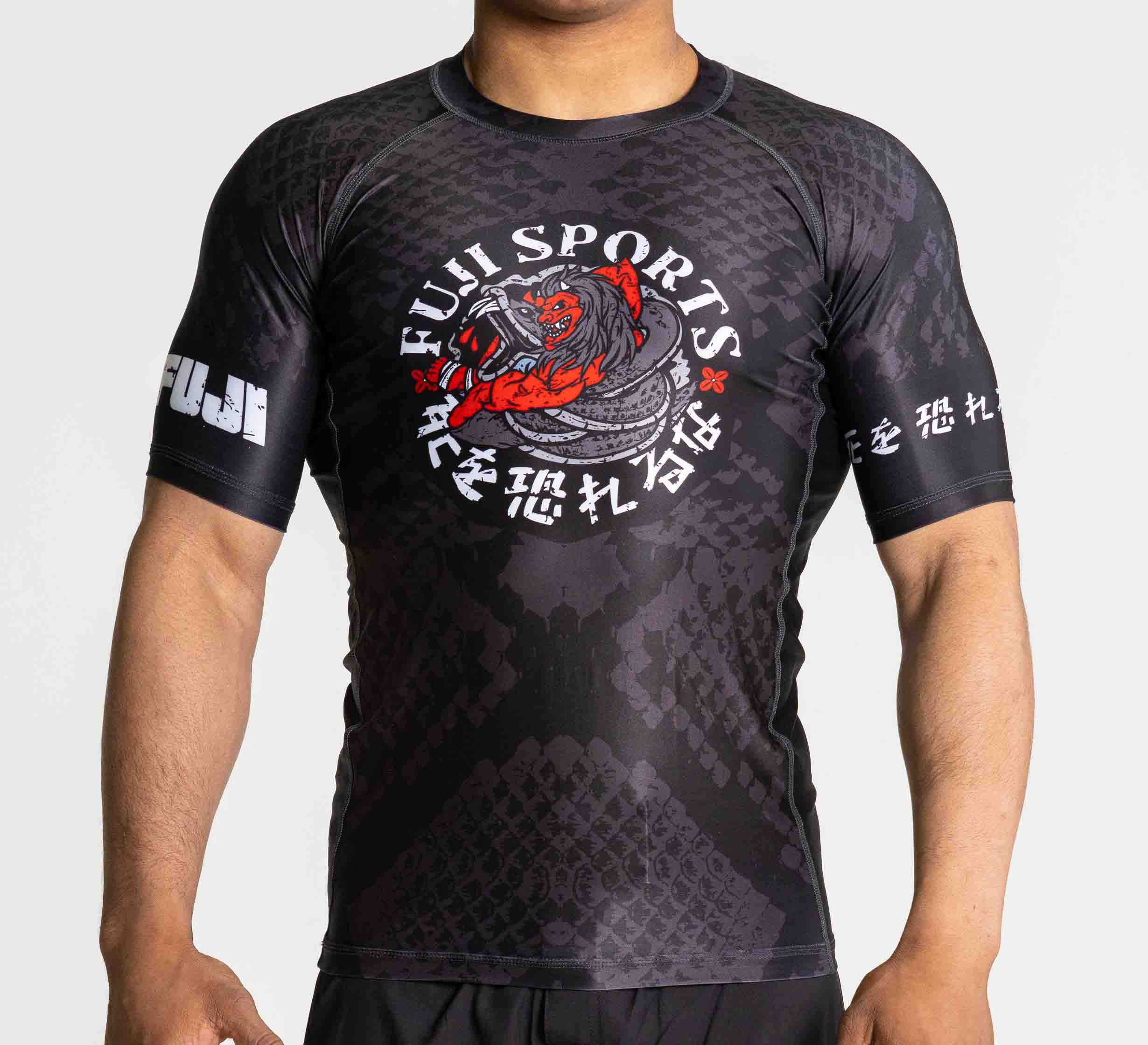 A person wears the Oni vs. Anaconda Short Sleeve Rashguard Black by FUJI Sports, featuring a striking red dragon graphic and