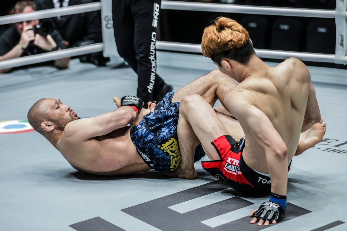 Masakazu Imanari attacking a leg lock entanglement during a no-gi grappling match, illustrating the position grapplers must learn to defend