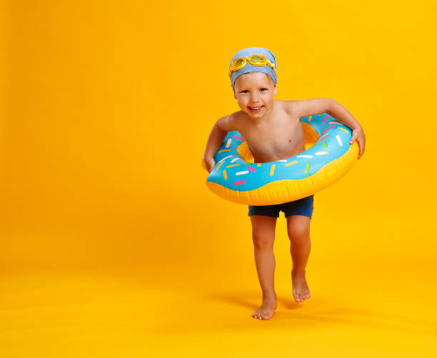 happy child boy in swimsuit with swimming ring donut on colored yellow background happy child boy in swimsuit with swimming r