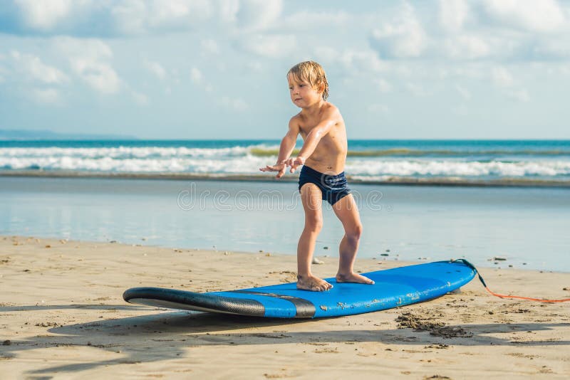 Little boy surfing on tropical beach. Child on surf board on ocean wave. Active water sports for kids. Kid swimming with surf