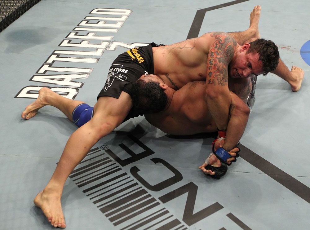 No-gi half guard transition in MMA cage with grappler defending sweep attempt