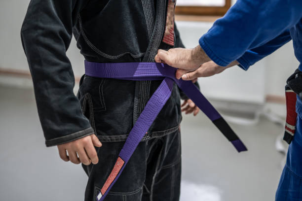 BJJ brazilian jui jutsu belt promotion close up on hands of unknown instructor black belt professor tie up purple belt on wai