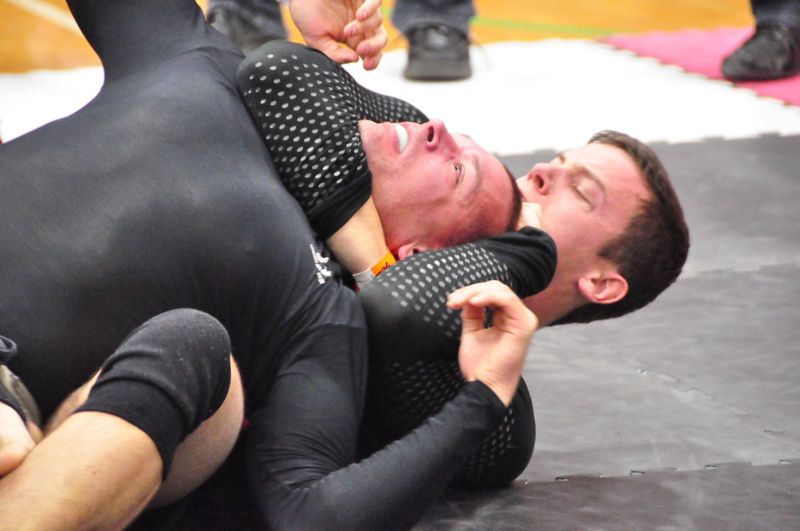 Two grapplers in black compression rashguards during a live no-gi rear naked choke