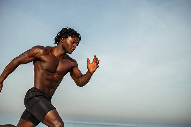 athletic male runner sprinting outdoors under a clear blue sky - athlete beach stock pictures, royalty-free photos & images