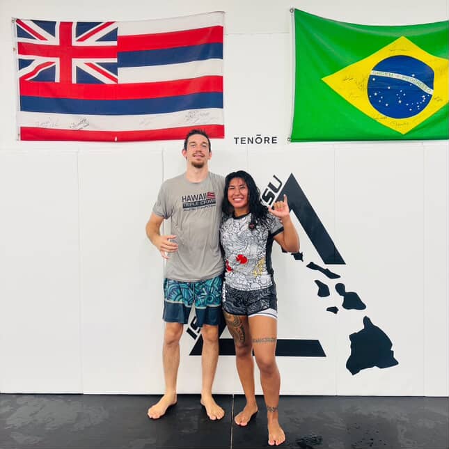 Female athlete wearing Rising Dragon white short sleeve BJJ rash guard practicing martial arts with male partner in gym