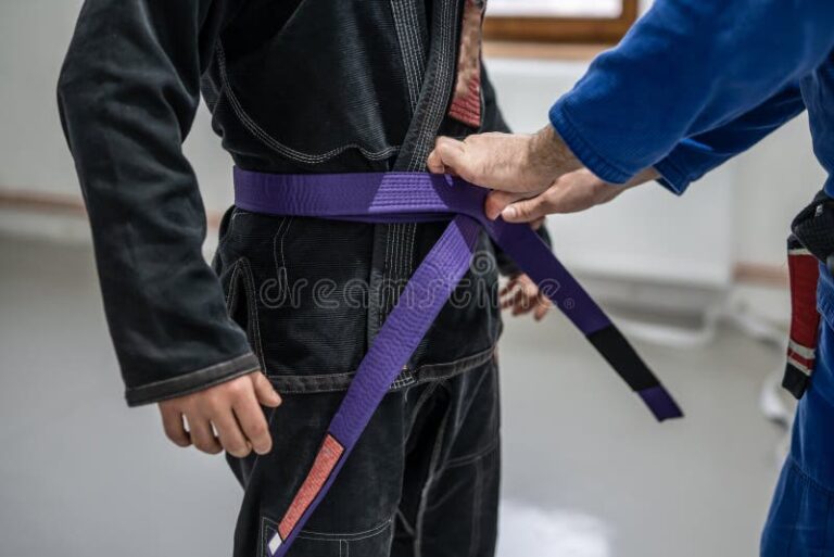 BJJ brazilian jui jutsu belt promotion close up on hands of unknown instructor black belt professor tie up purple belt on wai