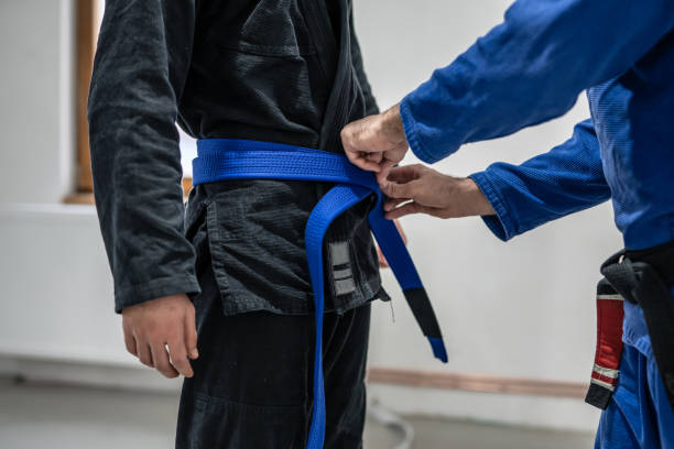 BJJ brazilian jui jutsu belt promotion close up on hands of unknown instructor black belt professor tie up blue belt on waist