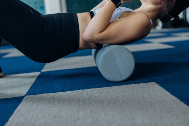 young woman using foam roller for stretching muscles - foam roller stock pictures, royalty-free photos & images