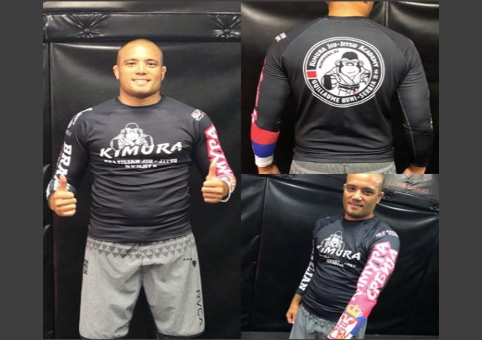 BJJ competitor wearing a properly fitted black compression rashguard, front view with thumbs up and back logo view showing tight torso fit