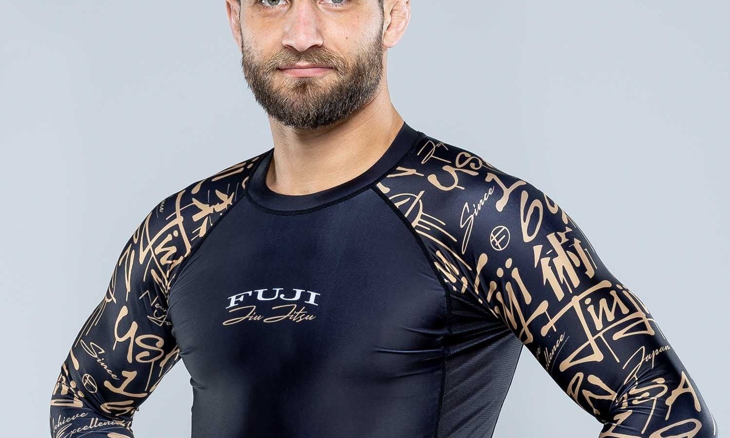 Grappler wearing a long-sleeve compression rashguard with hands on hips, showing torso length staying tucked at the waist