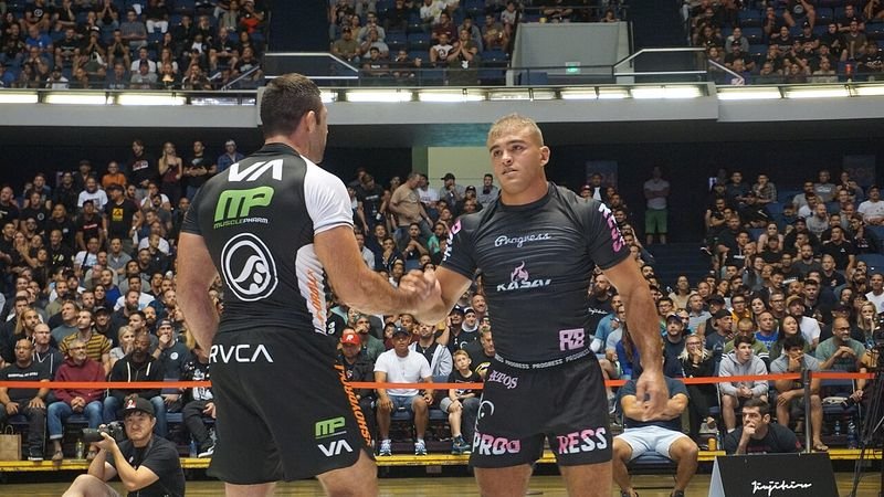 No-gi competitors shaking hands after a match, rashguards worn through a full event