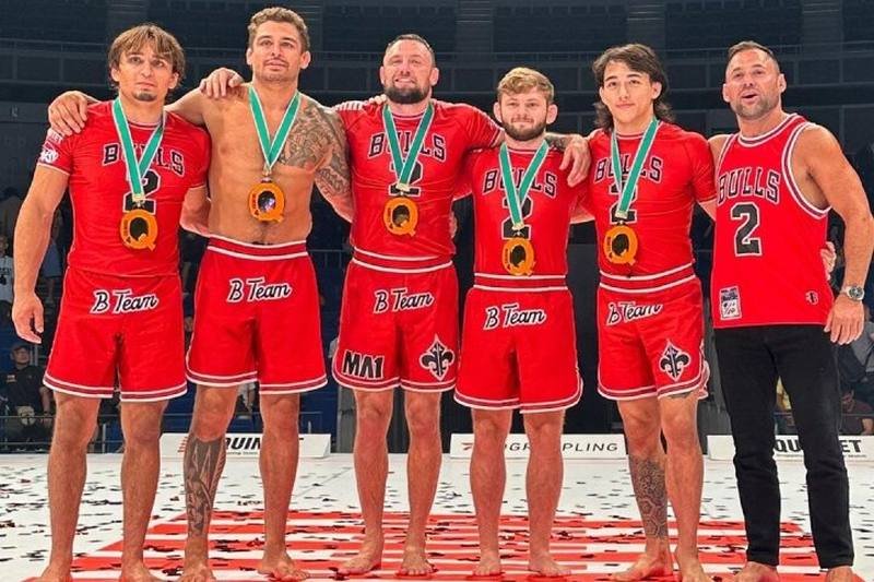B-Team grapplers celebrate in matching red no-gi rashguards after winning Quintet