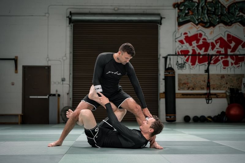 Grapplers drilling a leglock in fitted long-sleeve rashguards at a no-gi gym