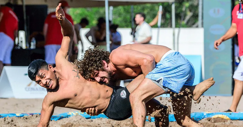 A grappler scoring a single leg takedown in a no-gi beach wrestling match