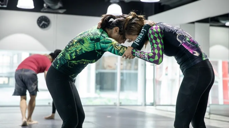 No-gi grapplers in rashguards clinched up in a collar tie before a takedown