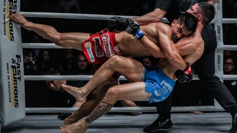 A fighter applying a no-gi style takedown against the cage in MMA competition