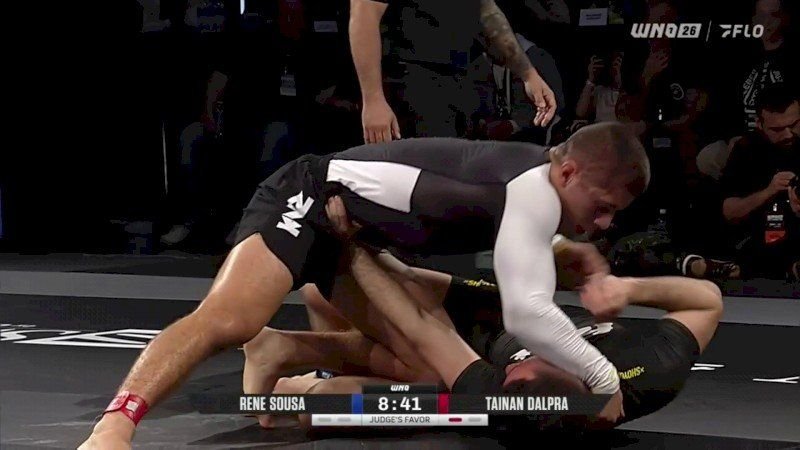 No-gi grappler driving chest-to-chest body lock pressure into an opponent's ribs during a guard pass