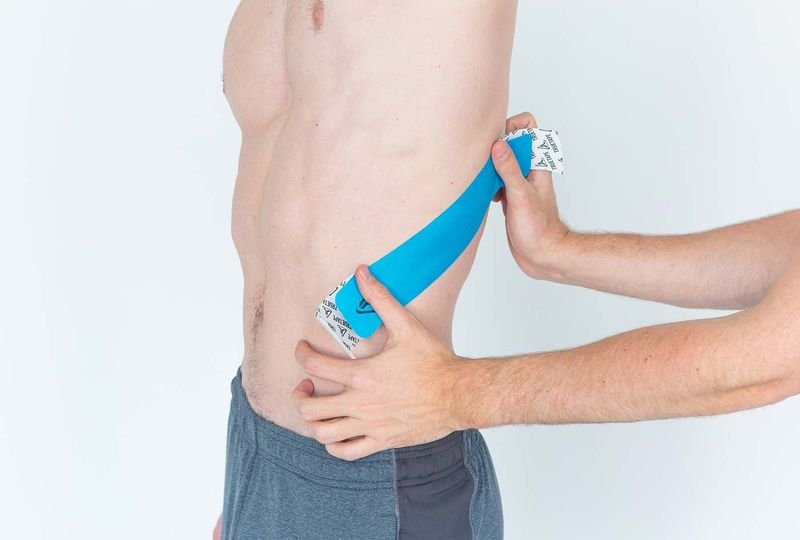 Applying kinesiology tape along the rib cage to support a grappling rib injury